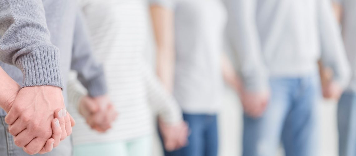 Group of caucasian people in bright clothes holding hands together